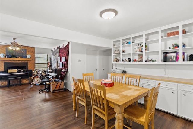 dining room with a large fireplace, ceiling fan, and dark wood-type flooring