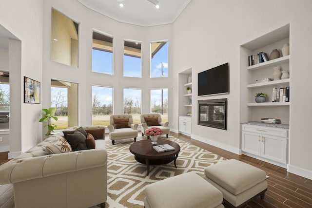 living room featuring built in features, dark wood-type flooring, a towering ceiling, and ornamental molding