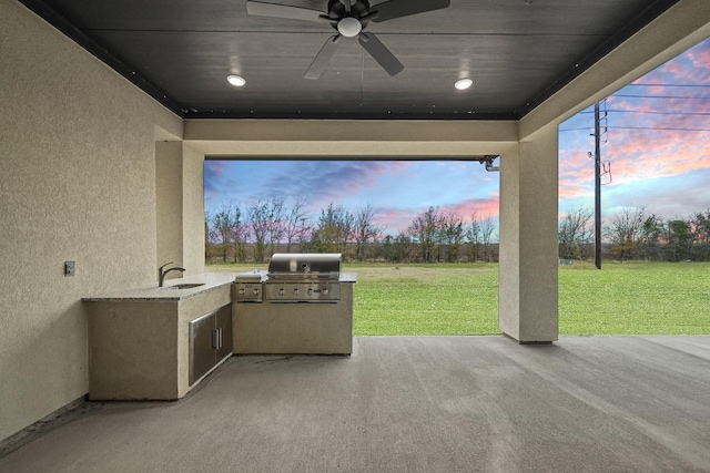 patio terrace at dusk featuring sink, exterior kitchen, a lawn, and ceiling fan