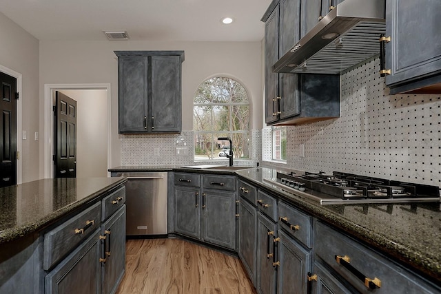 kitchen featuring sink, gray cabinetry, wall chimney range hood, dark stone countertops, and stainless steel appliances