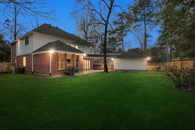 back house at dusk featuring a patio area, a lawn, and central AC