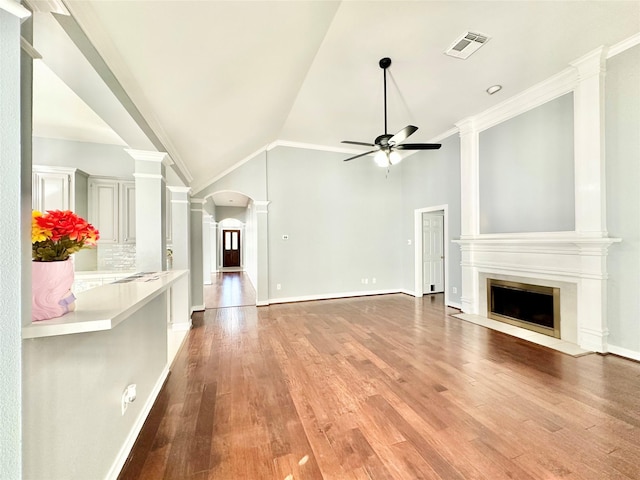 unfurnished living room with visible vents, arched walkways, lofted ceiling, a fireplace with flush hearth, and ornate columns