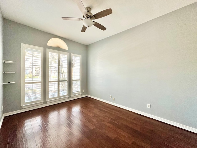 unfurnished room with dark wood-style flooring, a ceiling fan, and baseboards