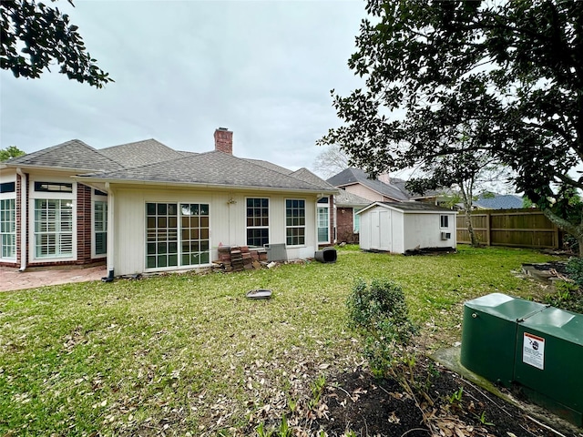 back of house with a yard, fence, a chimney, and a shed