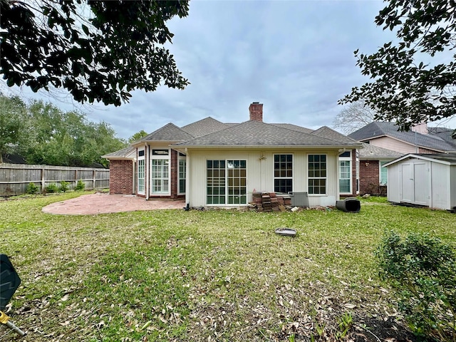 rear view of house featuring a chimney, fence, a yard, a patio area, and a shed