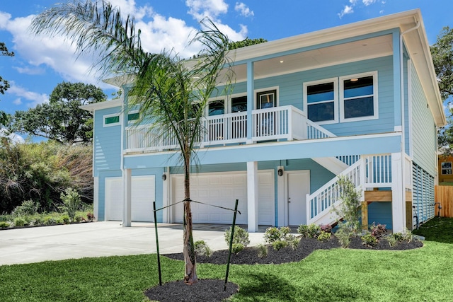 beach home with stairs, covered porch, a lawn, driveway, and an attached garage