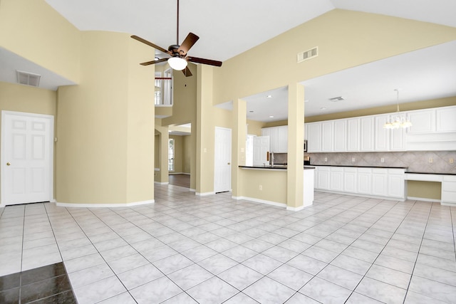 unfurnished living room featuring ceiling fan with notable chandelier, high vaulted ceiling, and light tile patterned flooring