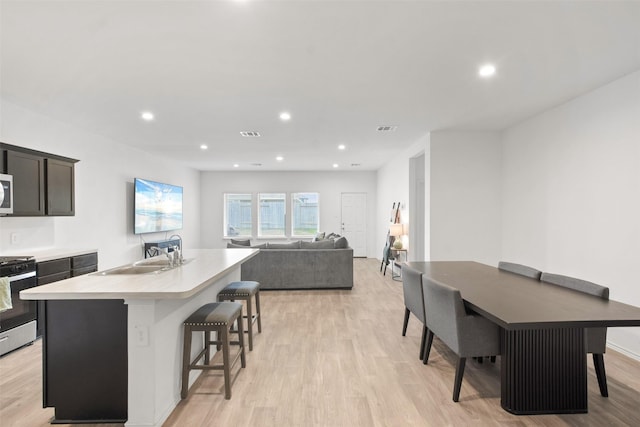 kitchen with stainless steel stove, a kitchen breakfast bar, sink, light hardwood / wood-style flooring, and an island with sink