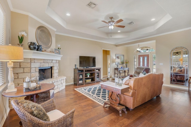 living room featuring a tray ceiling, wood finished floors, visible vents, and a ceiling fan