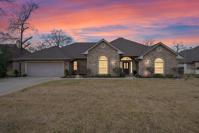 view of front of property featuring brick siding, a yard, an attached garage, and driveway