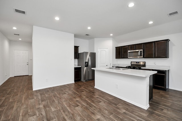 kitchen with appliances with stainless steel finishes, dark hardwood / wood-style flooring, an island with sink, sink, and dark brown cabinets