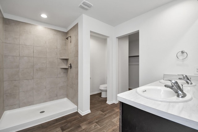 bathroom with wood-type flooring, tiled shower, toilet, and vanity