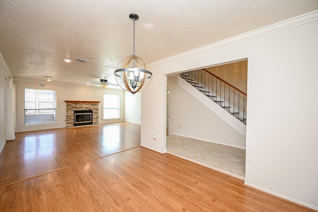 unfurnished living room with hardwood / wood-style floors, a textured ceiling, crown molding, and a stone fireplace