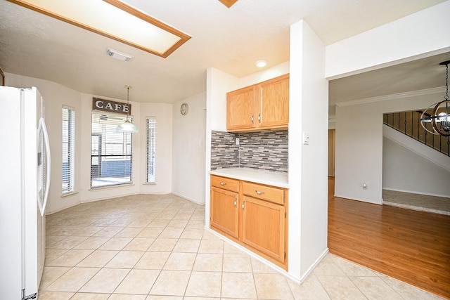 kitchen with tasteful backsplash, light tile patterned floors, decorative light fixtures, ornamental molding, and white refrigerator