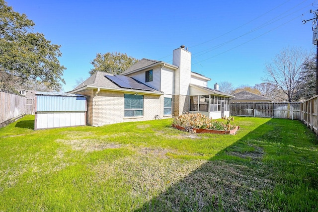 rear view of property featuring a lawn, solar panels, and a sunroom