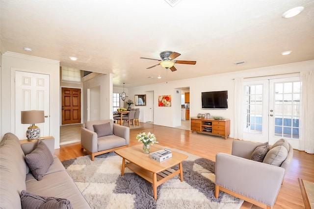 living room featuring crown molding, light wood-type flooring, ceiling fan, and french doors