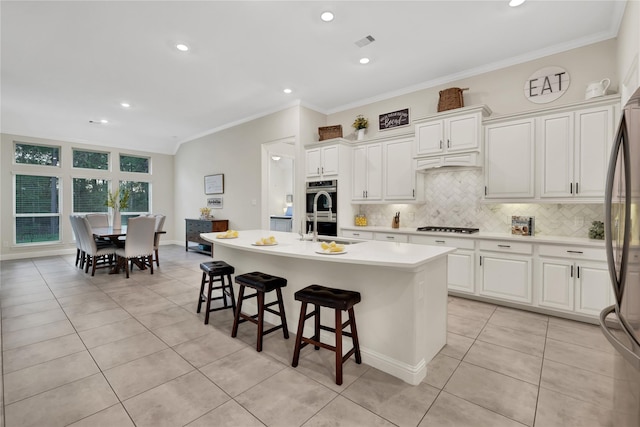 kitchen with a kitchen bar, white cabinets, sink, stainless steel appliances, and a center island with sink