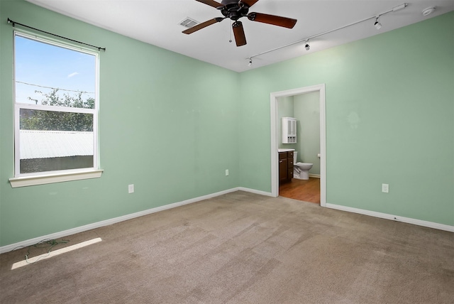 unfurnished bedroom featuring rail lighting, light colored carpet, connected bathroom, and ceiling fan