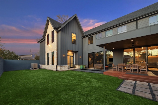 back house at dusk with a wooden deck and a lawn