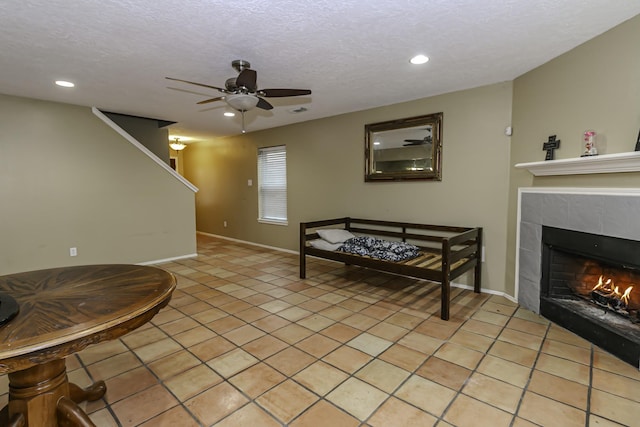 living room with ceiling fan, a textured ceiling, a fireplace, and light tile patterned flooring