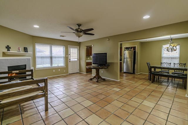 tiled living room featuring ceiling fan with notable chandelier, a wealth of natural light, and a high end fireplace