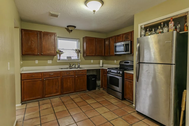 kitchen featuring sink, light tile patterned floors, appliances with stainless steel finishes, and a textured ceiling