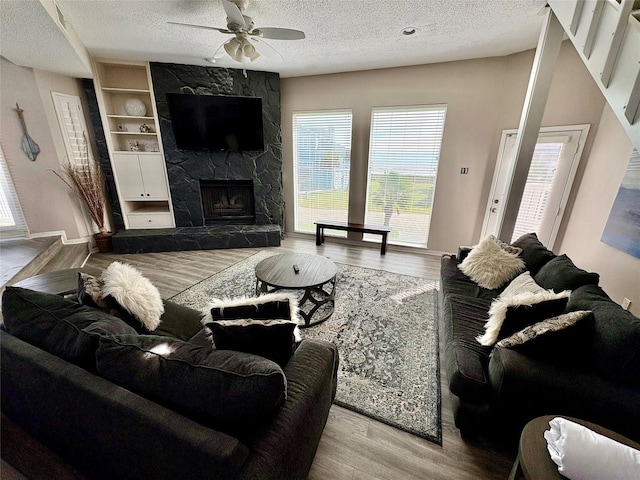 living room featuring a textured ceiling, built in features, a stone fireplace, and light hardwood / wood-style flooring