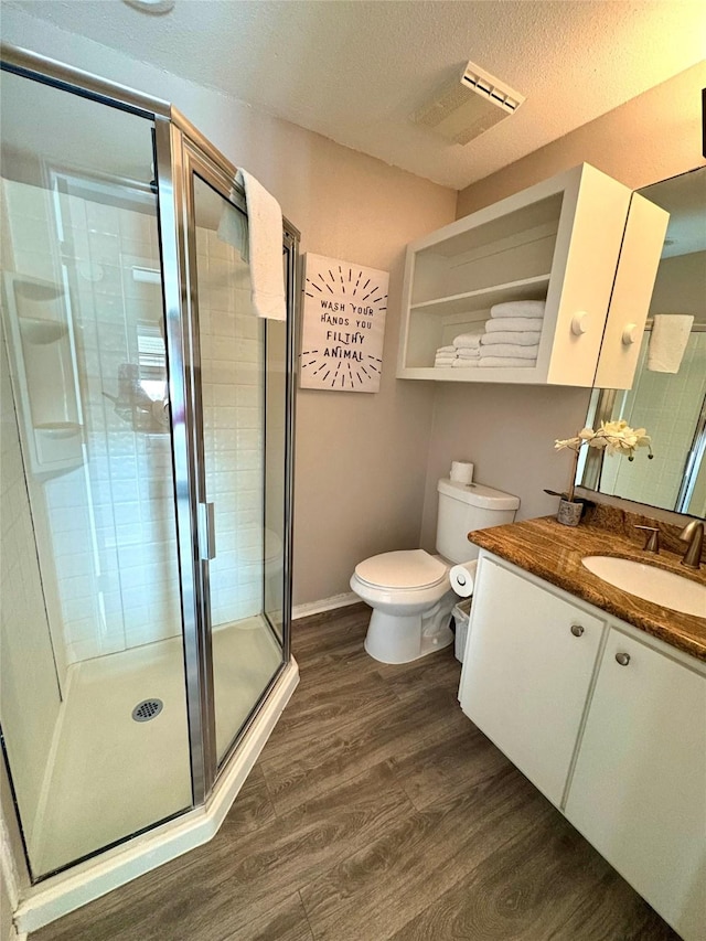 bathroom with hardwood / wood-style floors, a textured ceiling, vanity, toilet, and a shower with shower door