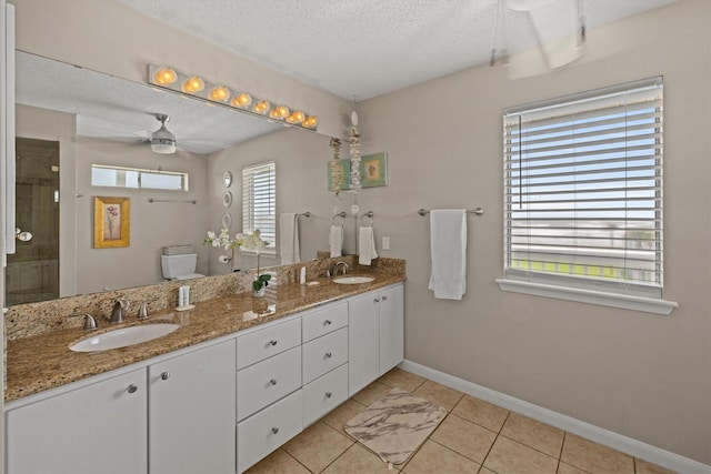 bathroom with a textured ceiling, tile patterned flooring, vanity, toilet, and ceiling fan