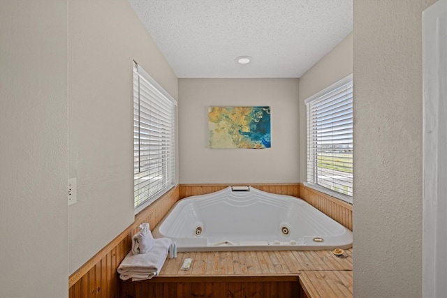 bathroom with a textured ceiling, a bath, and a healthy amount of sunlight