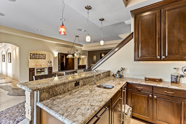 kitchen featuring decorative light fixtures, sink, kitchen peninsula, light tile patterned flooring, and light stone counters