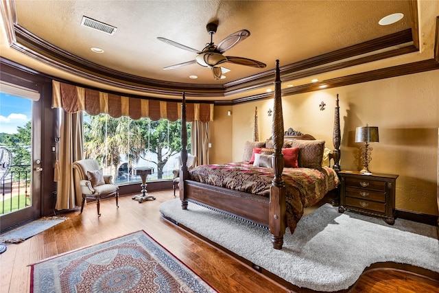 bedroom with wood-type flooring, access to outside, ceiling fan, a tray ceiling, and crown molding