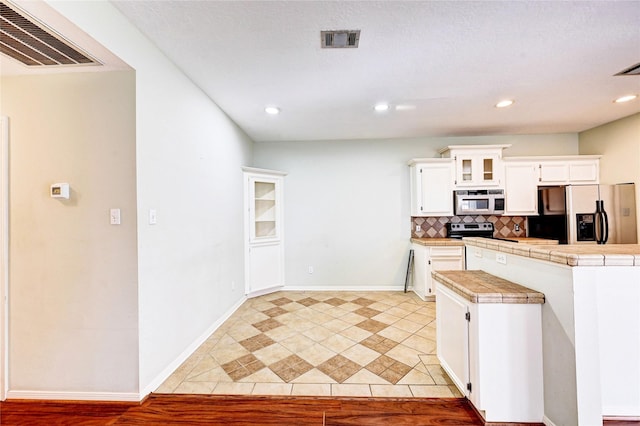 kitchen with tile counters, tasteful backsplash, white cabinetry, light tile patterned floors, and stainless steel appliances