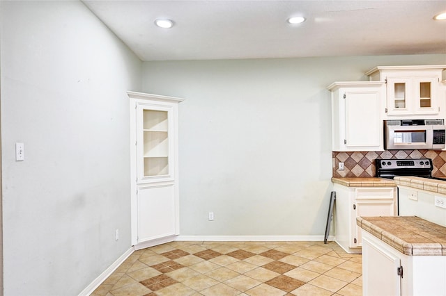 kitchen with tile counters, white cabinetry, light tile patterned floors, stainless steel electric stove, and backsplash