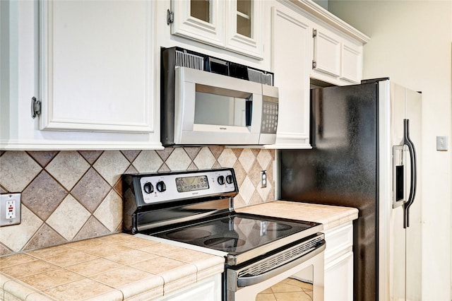 kitchen with stainless steel electric range oven, white cabinets, tasteful backsplash, and tile counters