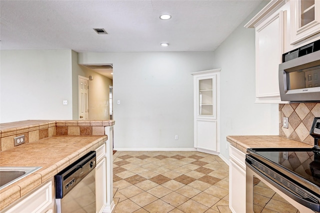 kitchen with tile counters, appliances with stainless steel finishes, white cabinetry, light tile patterned floors, and backsplash