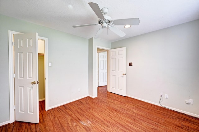 unfurnished bedroom featuring ceiling fan, light hardwood / wood-style floors, and a walk in closet