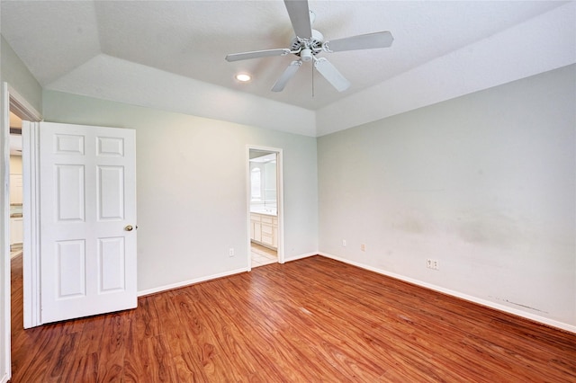 unfurnished bedroom with vaulted ceiling, wood-type flooring, a raised ceiling, ceiling fan, and connected bathroom