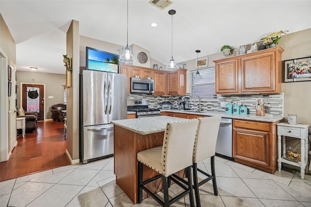 kitchen featuring a kitchen island, light stone counters, pendant lighting, and appliances with stainless steel finishes