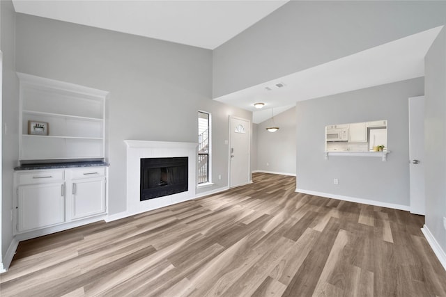 unfurnished living room with built in features, light hardwood / wood-style flooring, and lofted ceiling