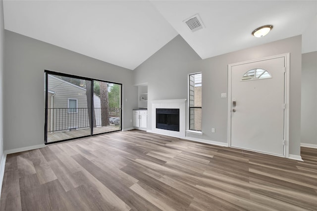 unfurnished living room featuring built in shelves, a tile fireplace, light hardwood / wood-style floors, and lofted ceiling