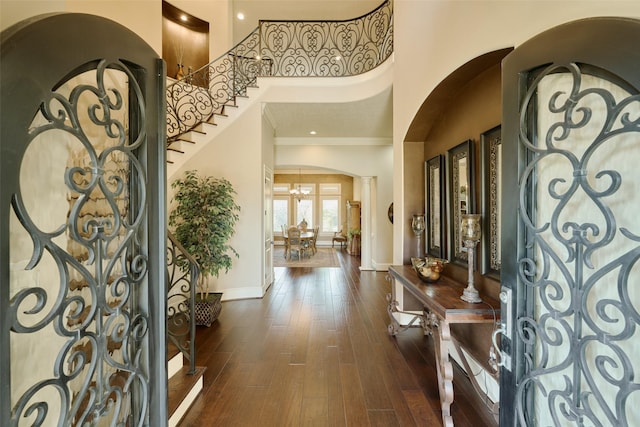 foyer entrance featuring dark wood-type flooring, a high ceiling, a notable chandelier, ornamental molding, and ornate columns