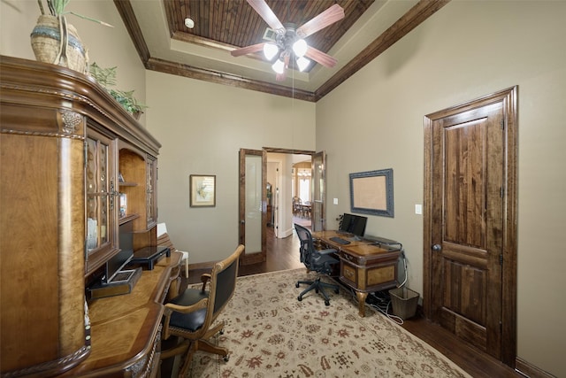 office space featuring dark wood-type flooring, ceiling fan, a towering ceiling, ornamental molding, and a raised ceiling