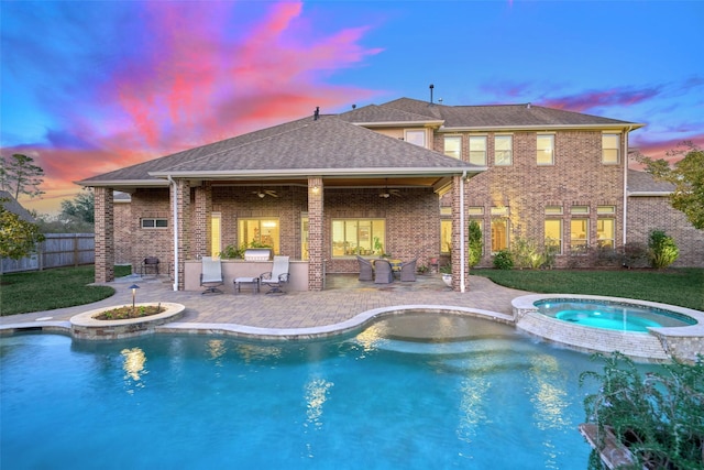 pool at dusk with an in ground hot tub, an outdoor kitchen, ceiling fan, and a patio area