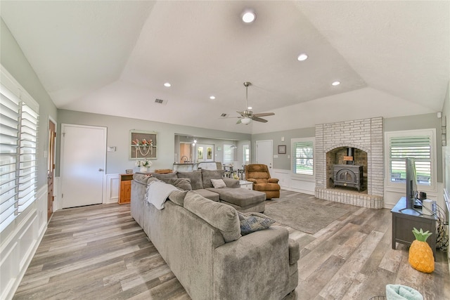 living room featuring vaulted ceiling, a tray ceiling, light hardwood / wood-style floors, and a wood stove