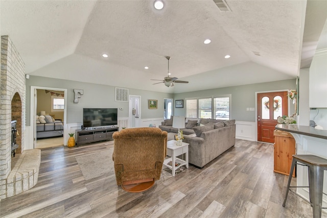 living room with ceiling fan, hardwood / wood-style flooring, vaulted ceiling, and a textured ceiling