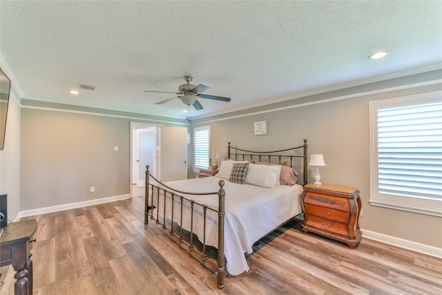 bedroom with a textured ceiling, wood-type flooring, ornamental molding, and ceiling fan