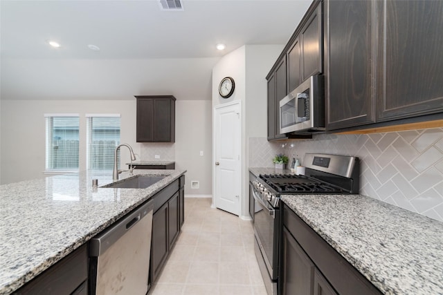 kitchen with appliances with stainless steel finishes, tasteful backsplash, sink, dark brown cabinets, and light stone counters