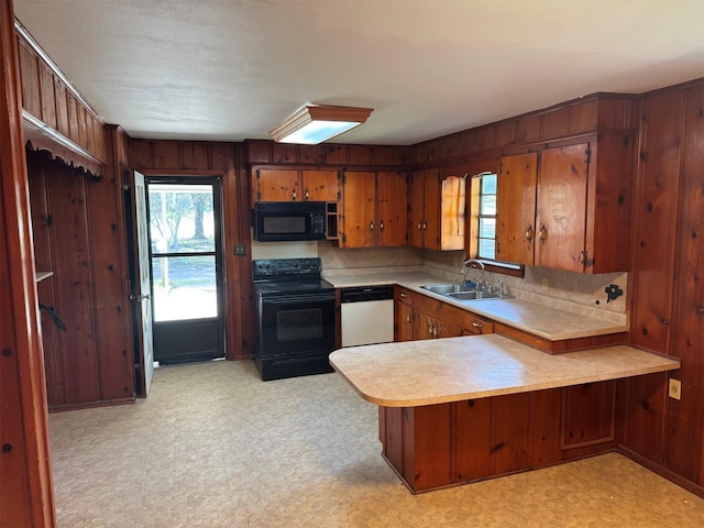 kitchen with kitchen peninsula, black appliances, wooden walls, and sink