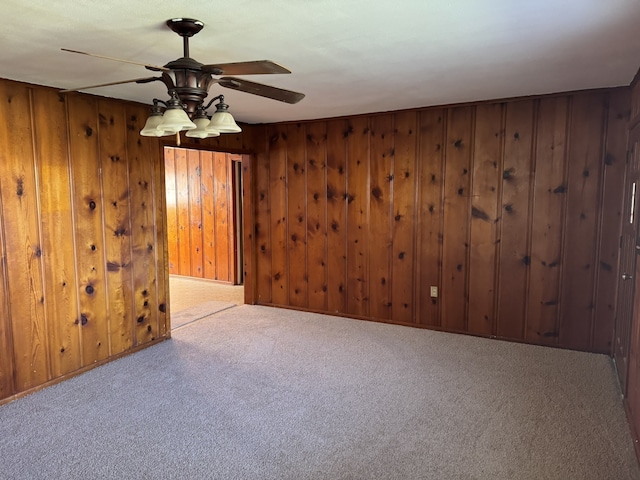 carpeted spare room featuring ceiling fan and wood walls